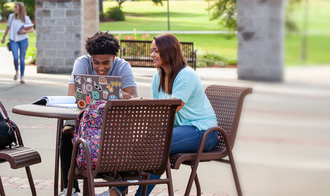 white female student and black male student sitting at an outdoor table reviewing notes